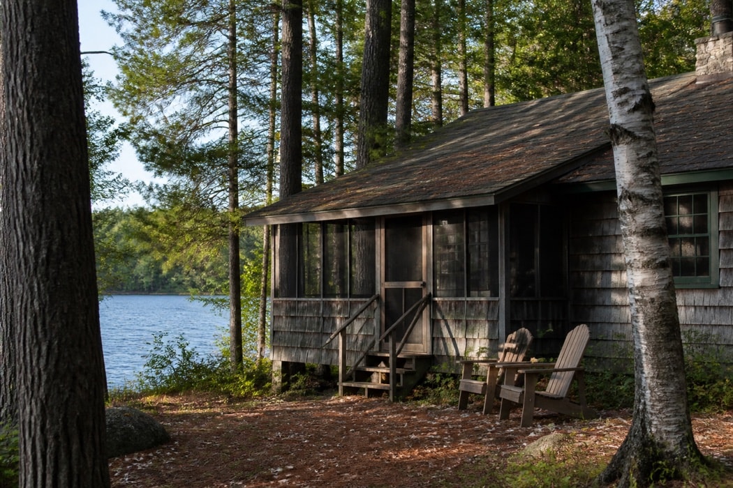 Modest cedar cabin among pine and birch trees beside a lake