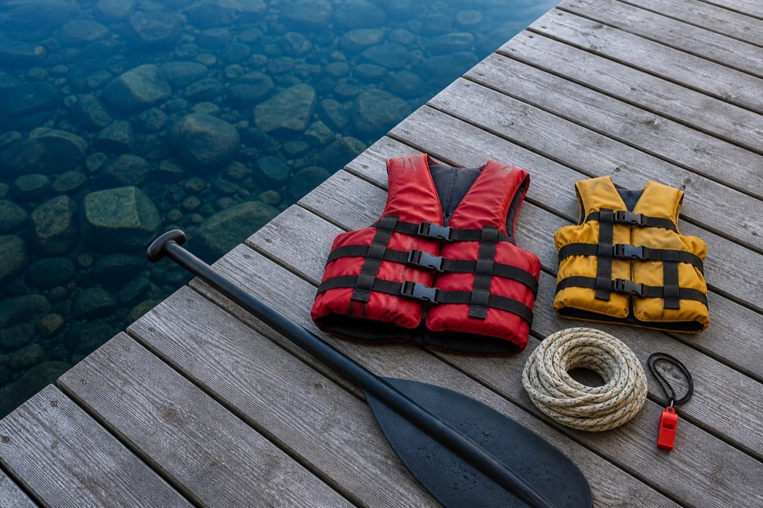 Life jackets, paddle, dock line and whistle arranged beside clear lake water